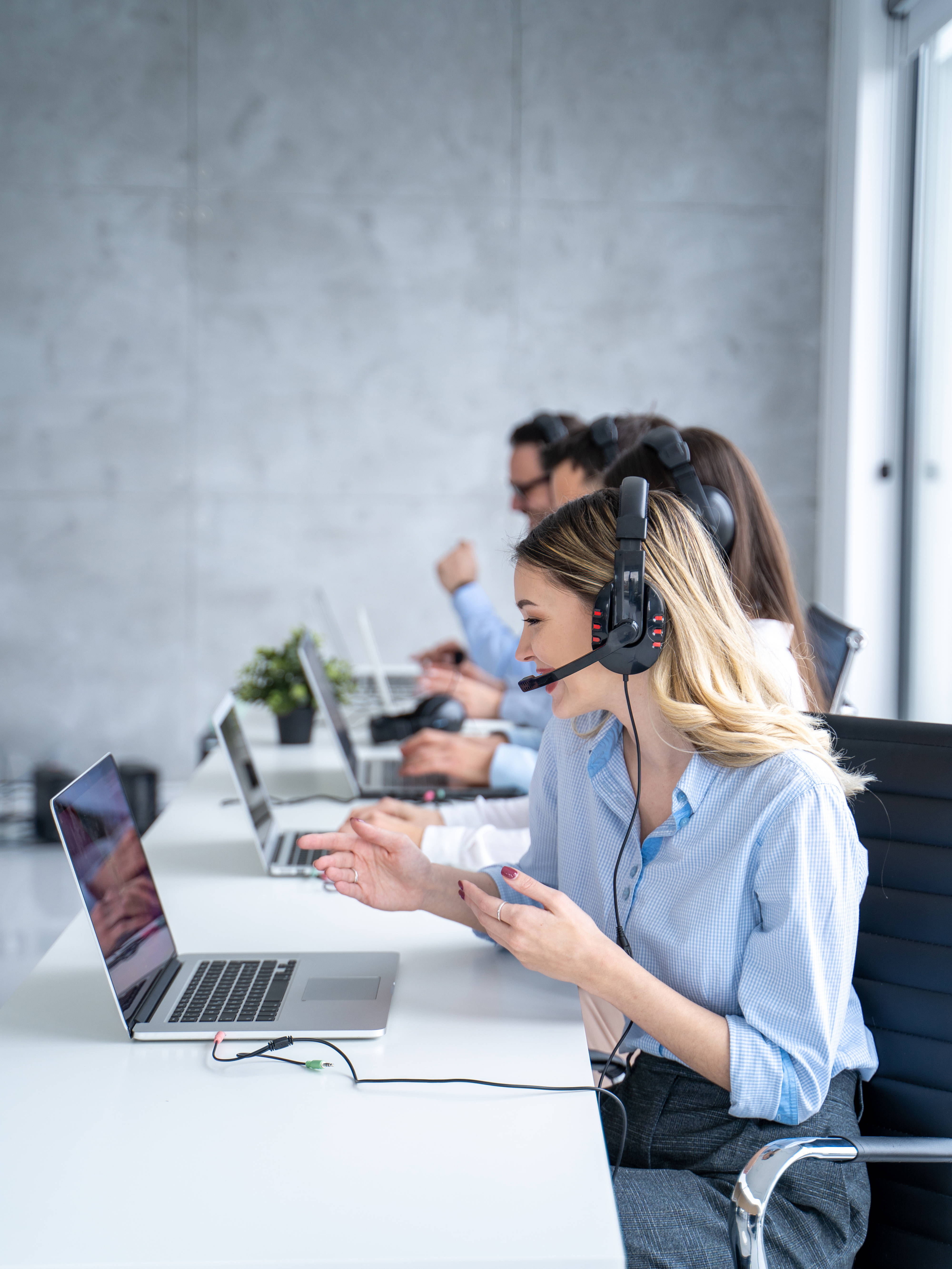 Vertical side view of beautiful blond hair call canter agent working with group of operators in office